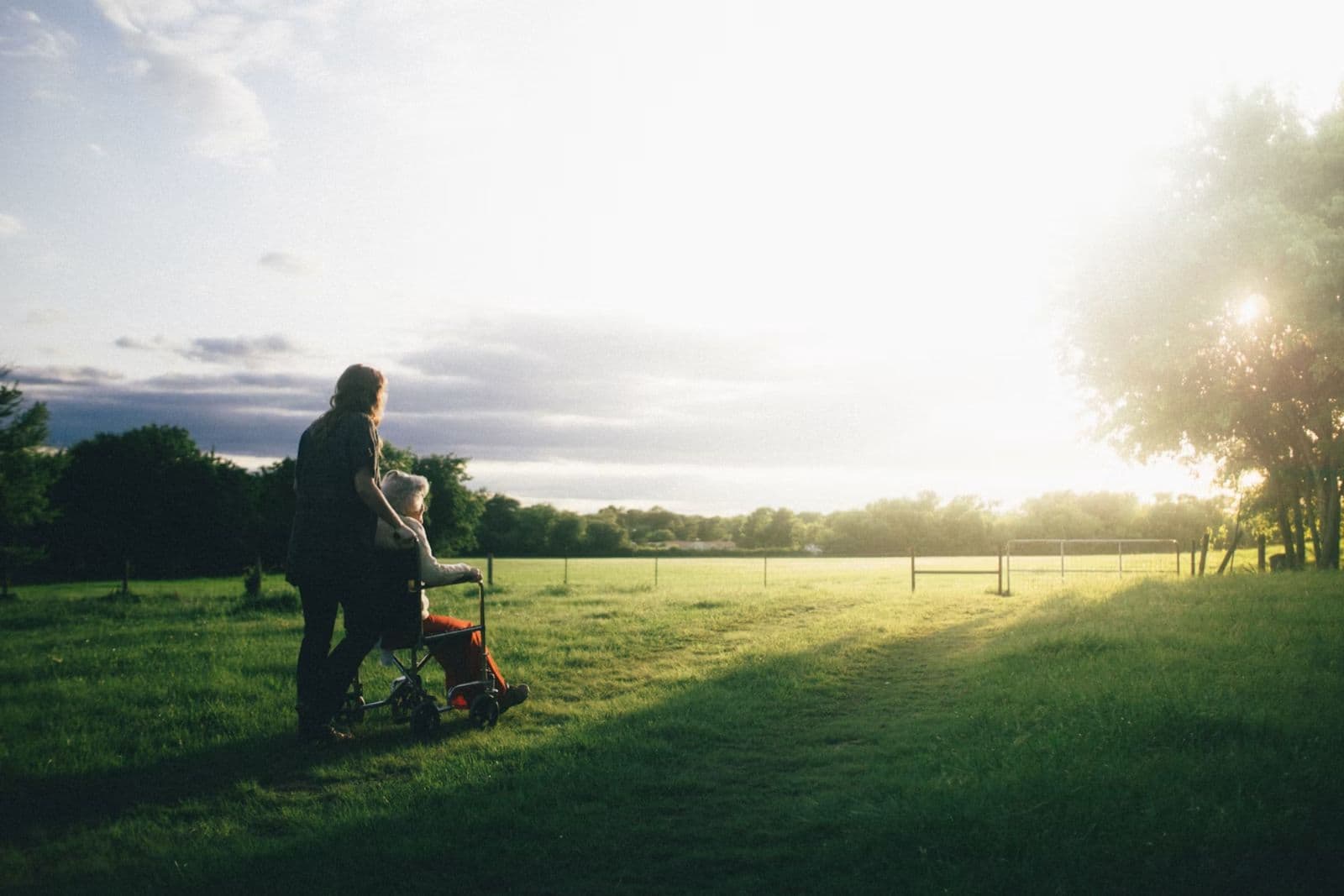 A caregiver walking outdoors with an older adult using a mobility aid